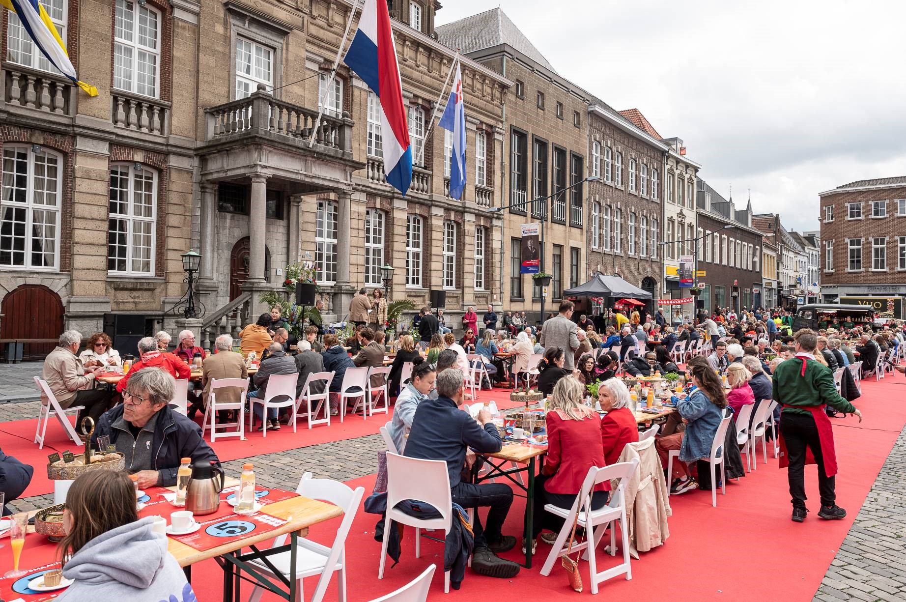 veel mensen zitten op witte stoelen aan tafels gedekt met eten en drinken